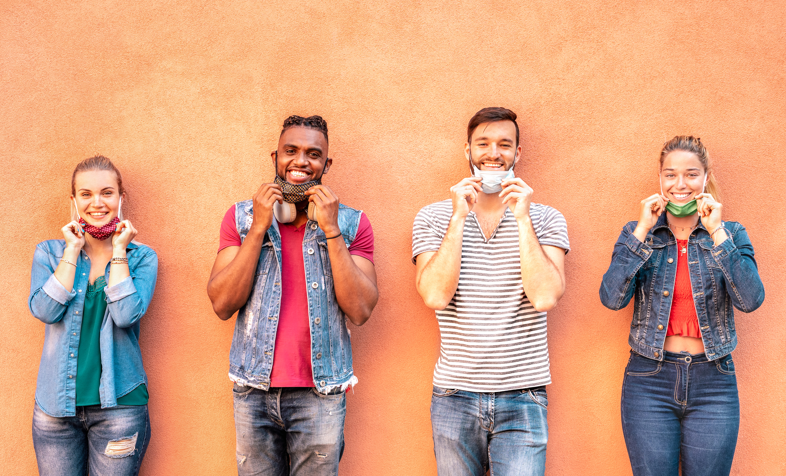 Four people standing in front of orange wall, and smiling.