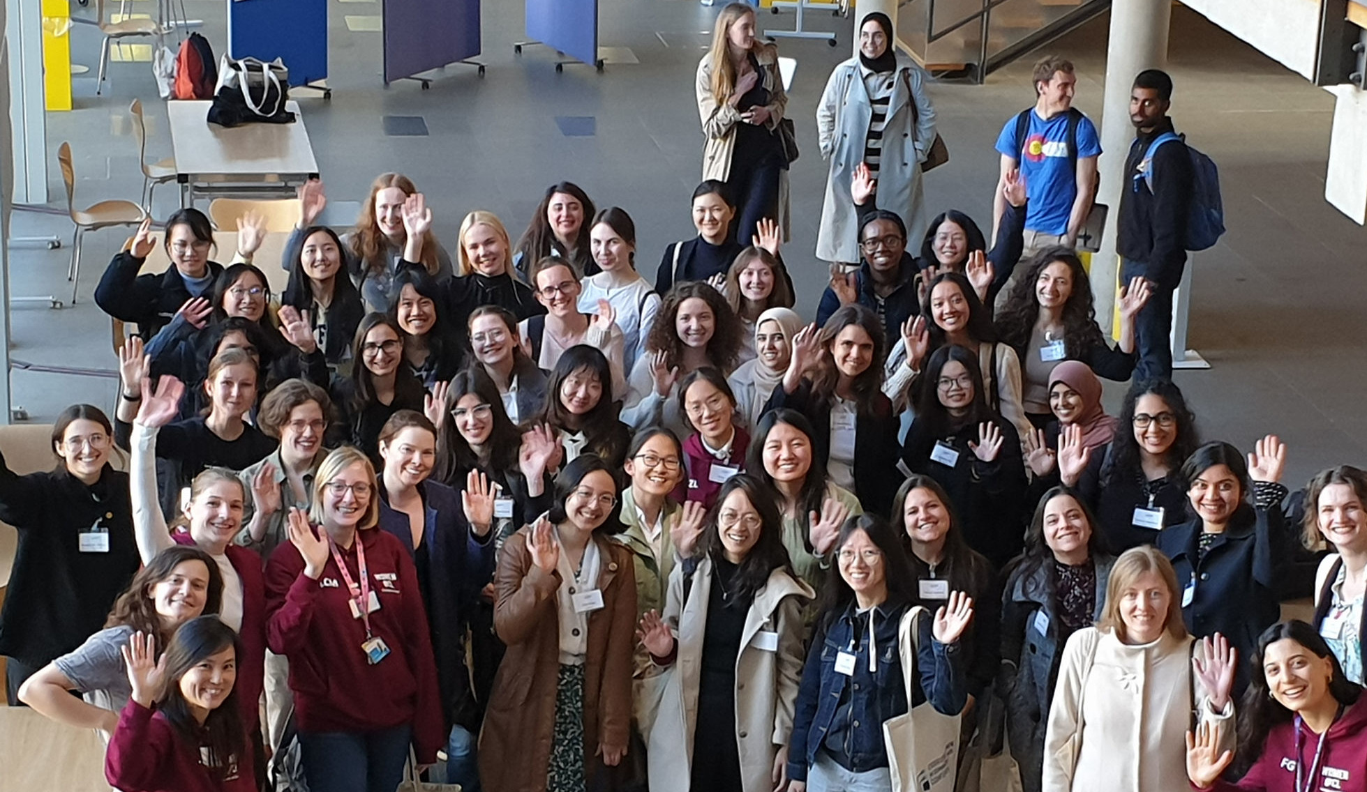 Large group of female computer scientists at a conference smiling and waving at the camera